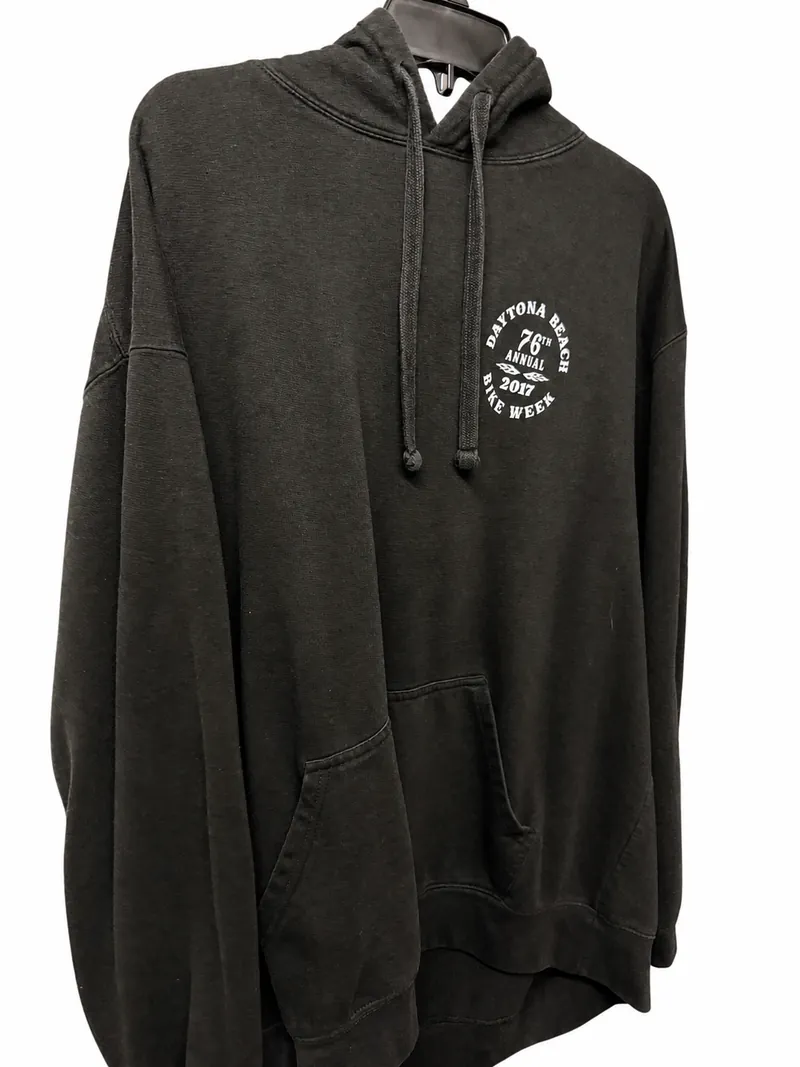 The front of the faded black hoodie on a hanger, with a small white circular Bike Week emblem on the chest.